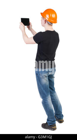 young engineer in a protective helmet with tablet computer in the hands of. Rear view people collection. backside view of person. Isolated over white background. Engineer tablet photographs something left. Stock Photo