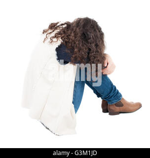 back view curly girl sitting and crying. girl relaxes. Rear view people collection. backside view of person. Isolated over white background. A girl in a white tank top sitting on the floor with his head resting on his legs. Stock Photo