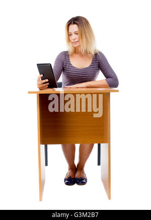 back view of woman sits by the table and looks at the screen of the tablet. Rear view people collection. backside view of person. Isolated over white background. front view of a girl behind office desk reading an e-book. Stock Photo