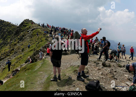 Landscape image of man taking a photograph amidst crowds of walkers on the  footpath to the summit of Mount Snowdon Stock Photo