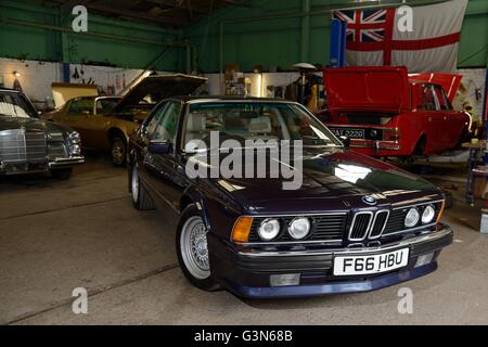 BMW 635 CSi standing in a classic car workshop with other British, American and German classic cars behind Stock Photo