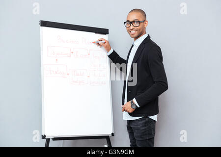 Smiling african young man in glasses writing business plan on flipchart Stock Photo