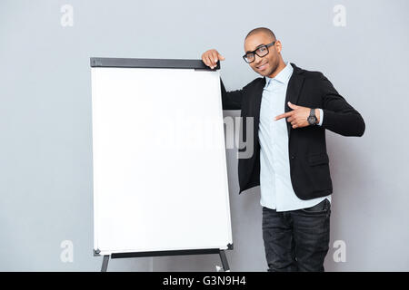 Happy african young man in glasses standing and pointing on blank flipchart Stock Photo