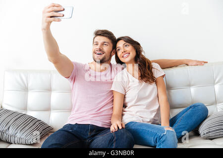 Beautiful young couple is making selfie using a smartphone smiling while sitting on sofa isolated on white background Stock Photo