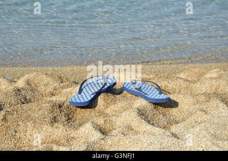 Pair of blue flip flops on a beach with sea in background Stock Photo