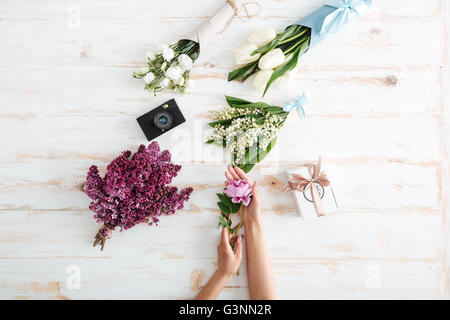 Hands of young woman with flower bouquets, gift box and photo camera on wooden table Stock Photo