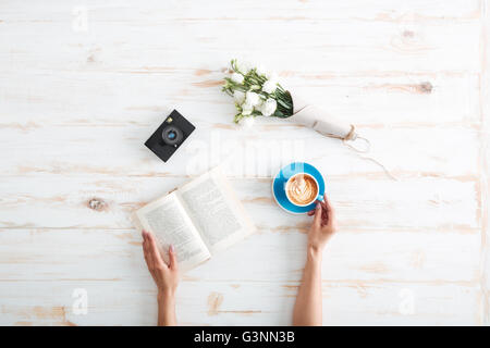 Female hands holding open book and coffee cup on the wooden desk Stock Photo