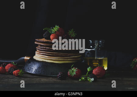 Ombre pancakes in the rusty pan with strawberries, blackberries and honey in dark backgound with mystical light Stock Photo