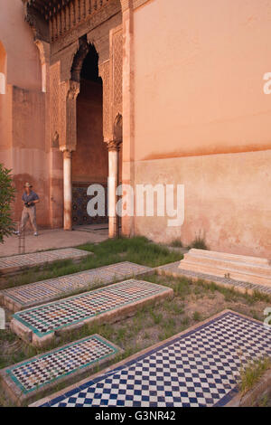 Tourist walks past tiled tombs outdoors at Saadien Tombs, Marrakech, Morocco, Africa Stock Photo