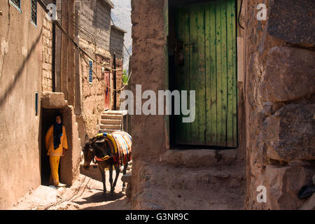 Green door on a mud clay home with a Berber woman emerging from her mud clay home to load her donkey in Ait Souka village Stock Photo