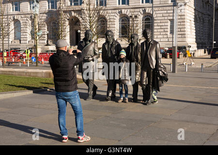 Merseyside, Liverpool, Pier Head Andrew Edwards’ Beatles statue outside Liver Building, visitors taking souvenir photograph Stock Photo