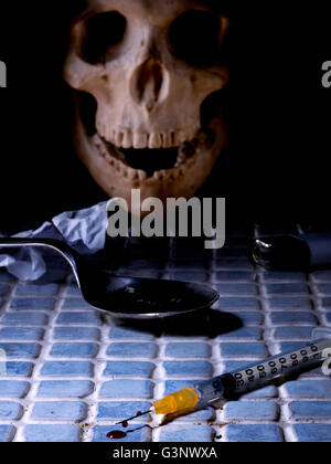 Syringe with drug on a dirty floor, and a skull at the bottom Stock Photo