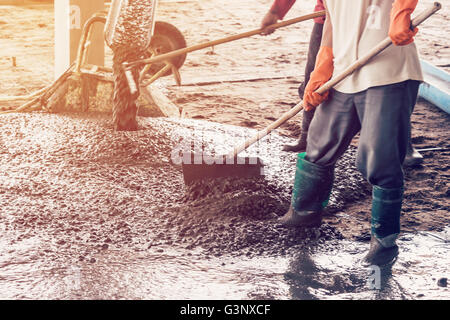 man workers spreading freshly poured concrete mix on building with vintage tone. Stock Photo