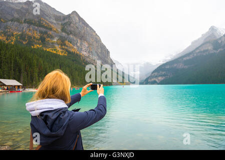 Beautiful girl taking photos with her phone in the Canadian mountains Stock Photo