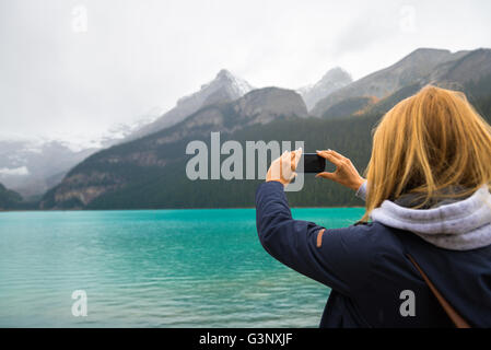 Beautiful girl taking photos with her phone in the Canadian mountains Stock Photo