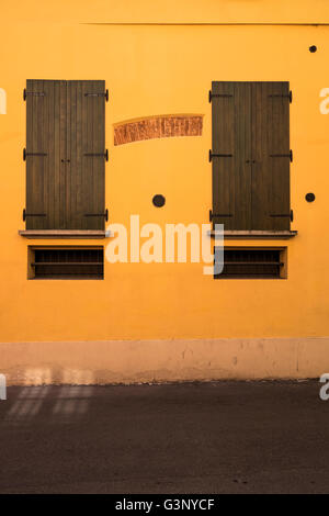 Detail of two wooden window shutters and red brick arch revealed through yellow wall in Bologna, Italy. Stock Photo