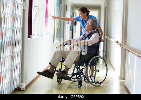 Female doctor carrying senior man on wheelchair in corridor Stock Photo