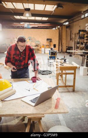 Carpenter using his smartphone while reading plans Stock Photo