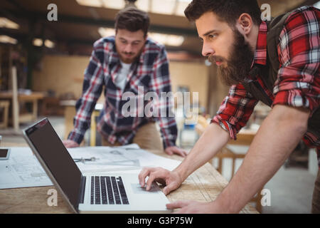 Carpenter using laptop while working on a blueprint Stock Photo