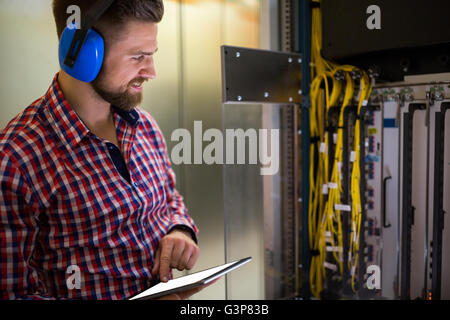 Technician in head phones using digital tablet while analyzing server Stock Photo