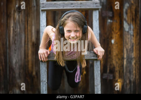 Happy little girl in headphones playing on the wooden stairs. Stock Photo