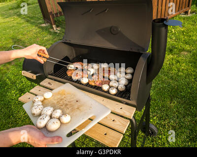 Red meat chops and champignons being placed on barbecue Stock Photo