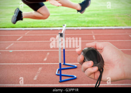 Composite image of coach is holding a stopwatch against assertive male athlete jumping above hedge Stock Photo