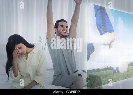 Composite image of man watching sport on television next to his bored wife Stock Photo