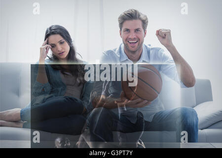 Composite image of man watching sport on television next to his bored wife Stock Photo