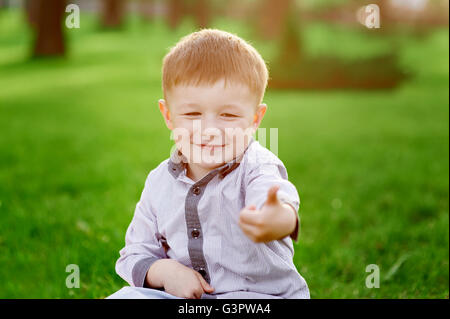 smiling boy sits on the green grass in the summer park Stock Photo