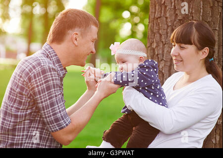 family parenthood concept - happy mother father and little girl playing in summer park Stock Photo