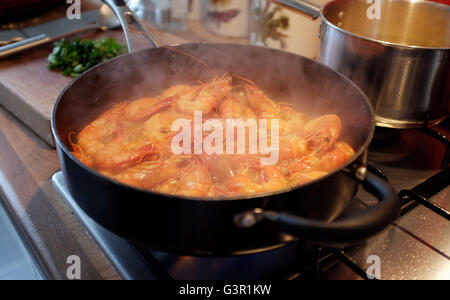 Hot steaming prawns being cooked in a frying pan with garlic chilli and white wine Stock Photo