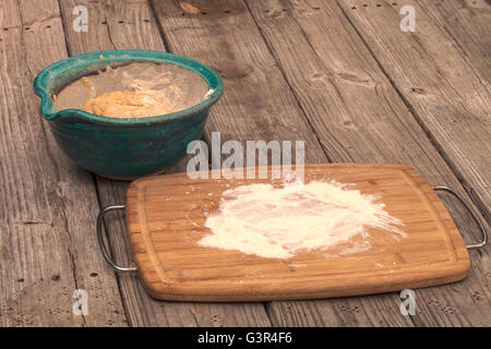 bread making series.  Bread dough rises in a bowl with a cutting board spread with flour on a rustic picnic table. Stock Photo