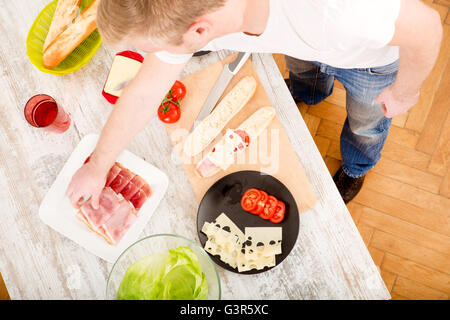 A young man preparing a sandwich in the kitchen. Stock Photo