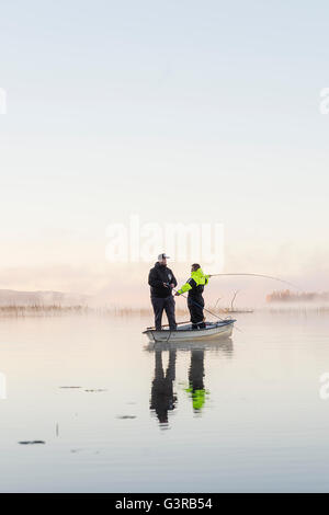 Sweden, Vastmanland, Bergslagen, Torrvarpen, Young men fishing in lake at sunset Stock Photo