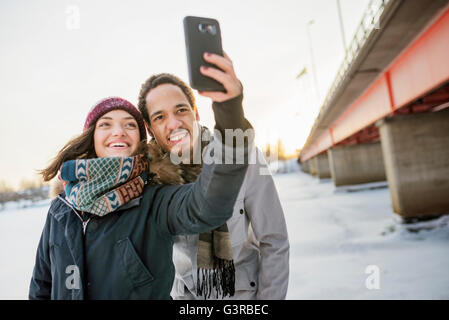 Sweden, Vasterbotten, Umea, Young couple taking selfie by bridge in winter Stock Photo