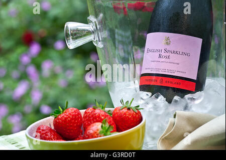 English Sparkling Rosé wine bottle in iced wine chiller with bowl of fresh strawberries on summer staycation alfresco floral table Stock Photo