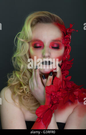 Gothic, fashion, fantasy, blonde English rose beauty portrait, red flowers, leaves, creative make-up Stock Photo