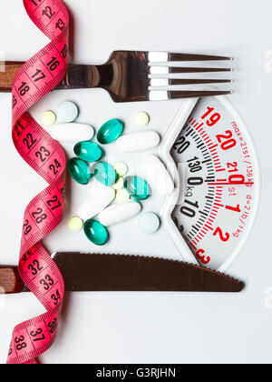 Healthy eating, medicine, health care, food supplements and weight loss concept. Pills with measuring tape on white scales Stock Photo