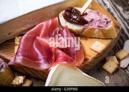 Cured ham and french bread with sundried tomato and meat liver pate. Antipasto platter on wooden board Stock Photo