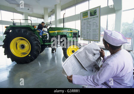 INDIA, Maharashtra, Pune, John Deere tractor dealer in village, John Deere tractor 5310 in showroom, farmer with newspaper , his son playing on tractor Stock Photo
