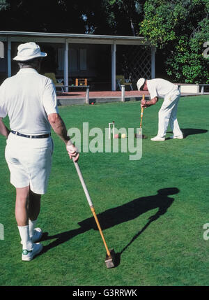 The traditional game of croquet is a popular activity for members of the the local croquet club who dress in all white apparel, as well as for guests at The Inn at Rancho Santa Fe, both of whom play on the sprawling front lawn of that luxury hotel in San Diego County, California, USA. Club members follow the official rules of the U.S. Croquet Association for Six-Wicket American Croquet that specify the equipment to be used, including the mallets, balls, wickets and stake. Here a male club player strikes his yellow ball with a square wooden mallet into an opponent's red ball. Stock Photo