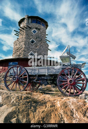 A wagon that is a relic of the Old West sits in front of the Desert View Tower that opened in 1920s as a roadside attraction and rest stop on a desolate section of cross-country highway near Mexico in Imperial County in Southern California, USA. Strong winds often buffet the observation deck atop the 70-foot (21-meter) hand-built stone structure that is in the In-Ko-Pah Mountains at an elevation of 3,000 feet (914 meters). This remote one-of-a-kind tower is surrounded by boulders bizarrely painted with folk art faces of reptiles, animals and other creatures. Stock Photo