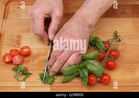 Closeup of hands chopping basil and tomatoes on a wooden chopping board Stock Photo