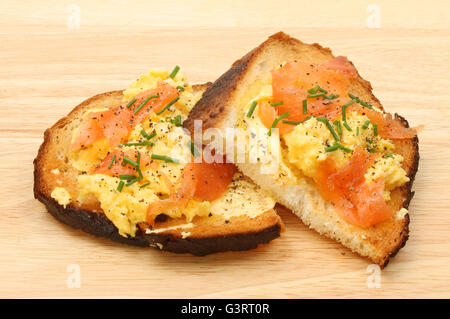 Scrambled egg with smoked salmon and chives on toasted crusty bread on a wooden board Stock Photo