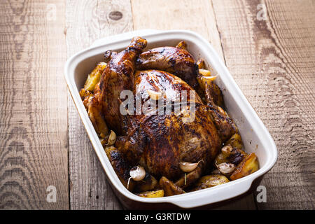 Homemade whole roasted chicken with with garlic and potatoes in ceramic pan, high angle view Stock Photo