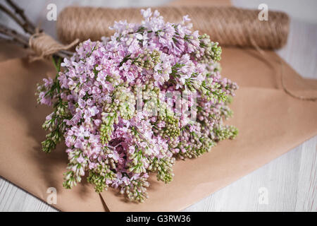 Empty postal envelope and bouquet of lilac flowers on the white wooden background, copy space. Top view. Stock Photo