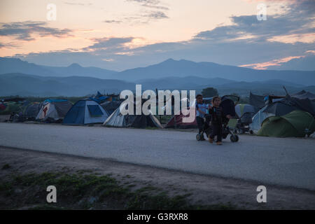 Two young girls push a stroller with their baby sister on the road through Idomeni refugee camp for Syrian refugees in Greece. Stock Photo
