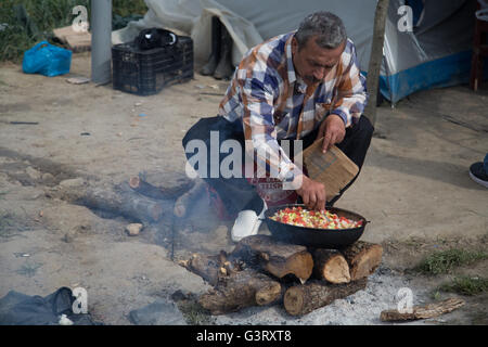 A Syrian Kurdish man cooks on logs and fire in the Syrian refugee camp of Idomeni in Greece, near the Macedonian border. Stock Photo