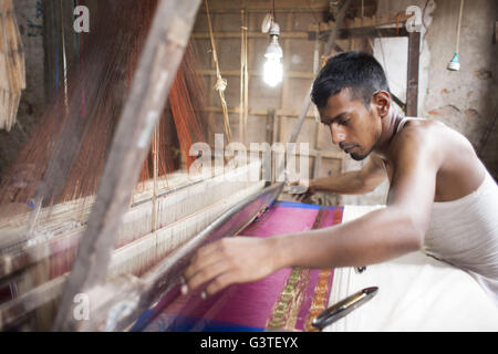 Dhaka, Bangladesh. 15th June, 2016. Handloom weaver weaves Banarasi saree on a traditional wooden hand weaving loom at Mirpur Banarasi Palli, in Dhaka, Bangladesh. Business in Mirpur Banarasi Palli, a market place well-known for different kinds of traditional Banarasi Sarees in Bangladesh, is facing tough times. People, who used to go there to purchase the famous Banarasi sarees, are increasingly opting for trendy Indian sarees. The popularity of these custom-made sarees is losing its charm as colorful Indian chic sarees are more in demand among local buyers. The Benarasi saree, whose history Stock Photo